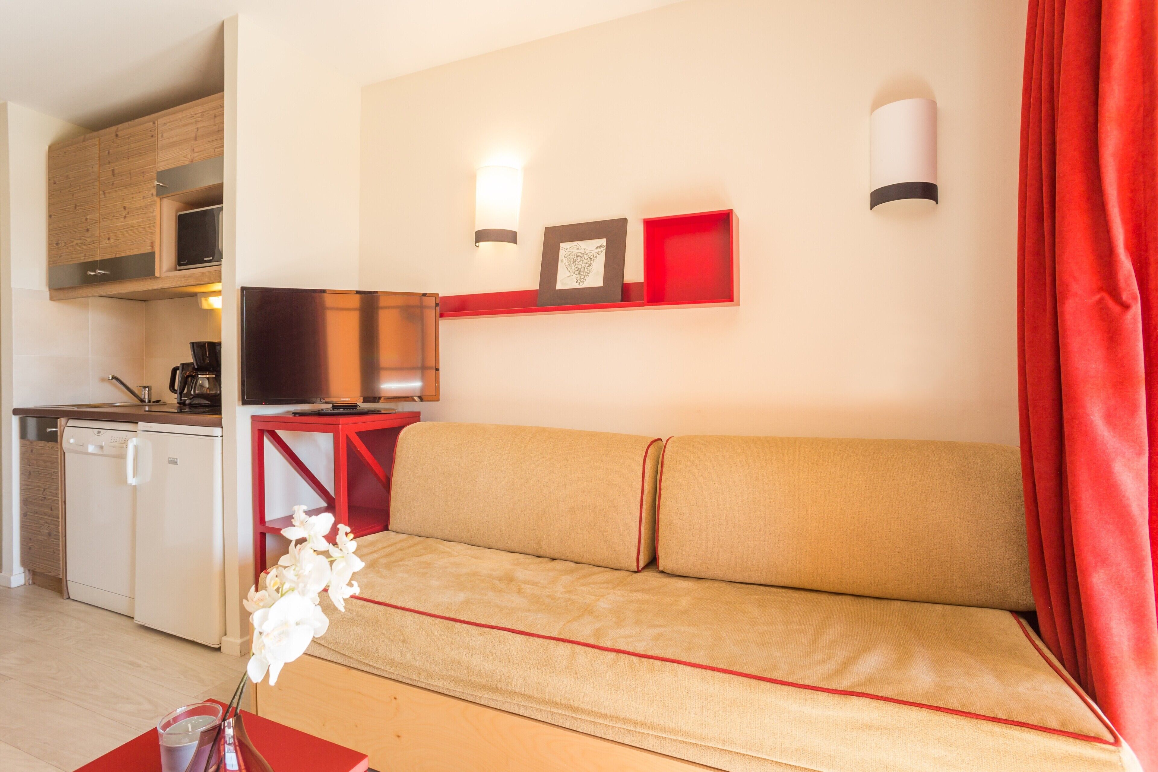 A compact living space with a sofa, a small kitchenette, and a red accent wall.