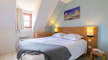 A bedroom with a bed, a nightstand, a lamp, a window with curtains, and a painting on the wall.