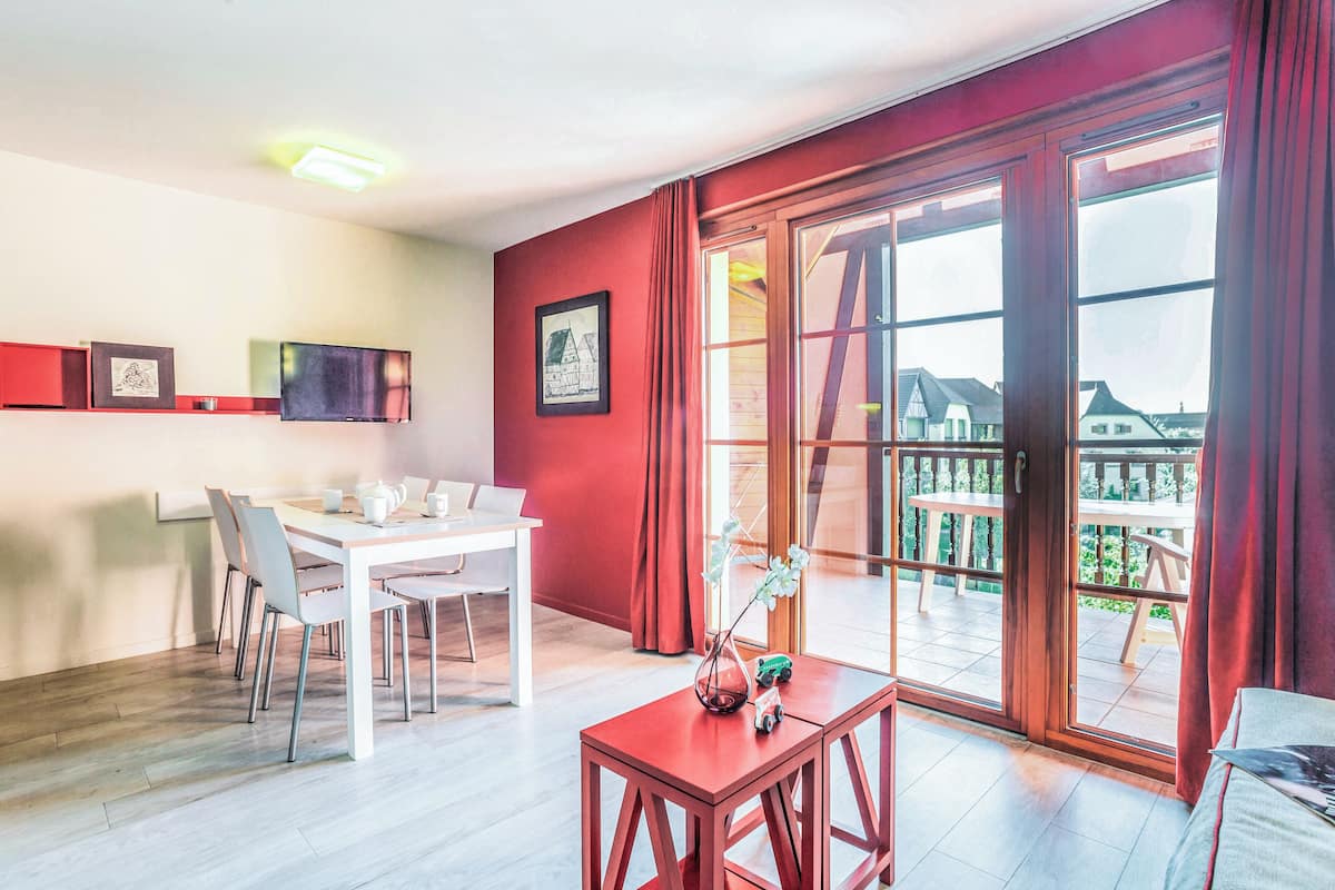 A modern room with a dining area, a large window with a view, and a red accent wall.