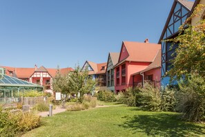 A row of colorful buildings with red and blue facades, surrounded by green lawns and trees. - Pierre & Vacances Résidence Le Clos d'Eguisheim (Eguisheim)