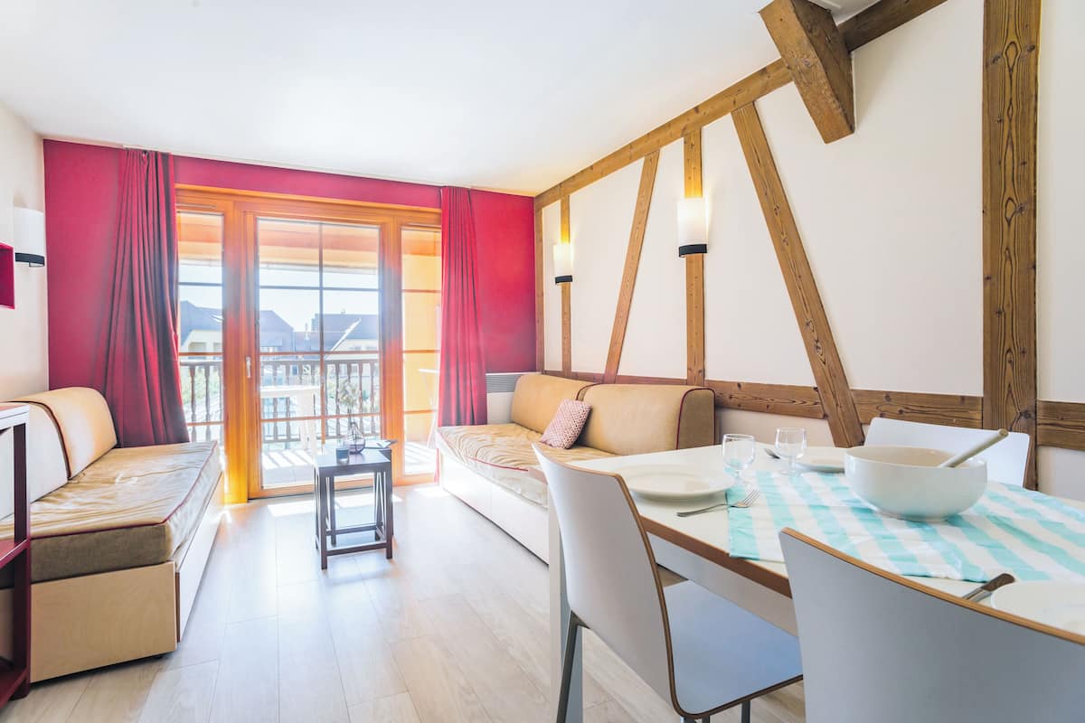 A modern room with a sofa, dining table, and chairs. There is a balcony with a view of buildings.
