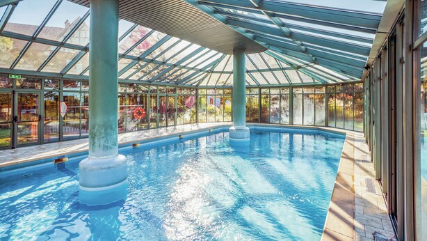 An indoor swimming pool with a glass ceiling, clear water, and tiled floor. - Pierre & Vacances Résidence Le Clos d'Eguisheim (Eguisheim)