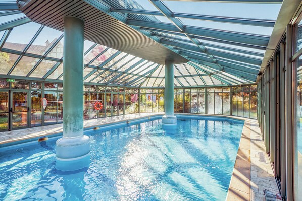 Una piscina techada, sombrillas, sillones reclinables de piscina