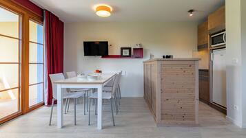 Una cocina moderna con una isla de madera, un comedor con sillas blancas y un amplio ventanal con cortinas rojas.