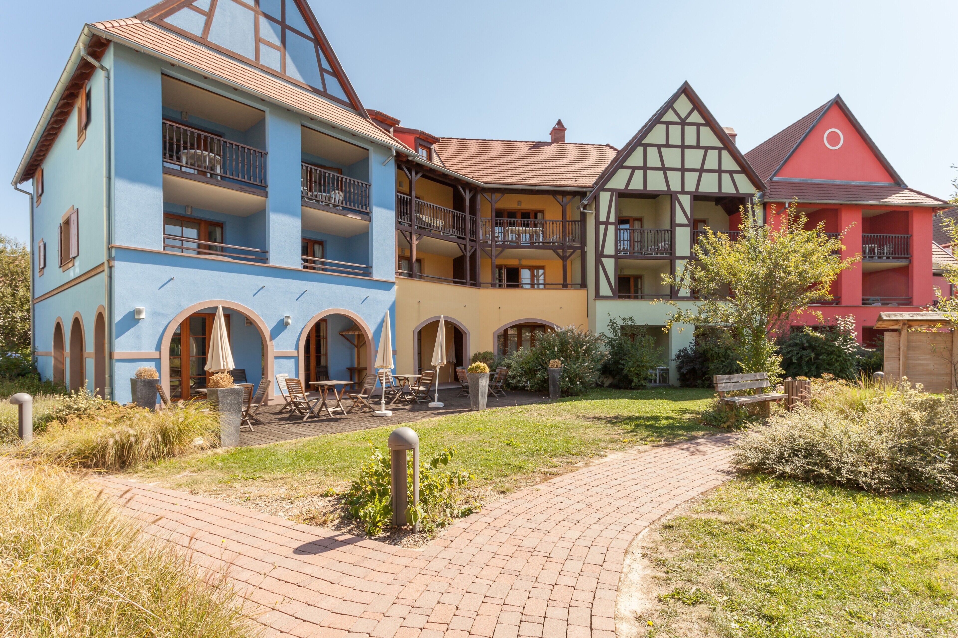 A multi-story building with balconies, a brick pathway, and outdoor seating.