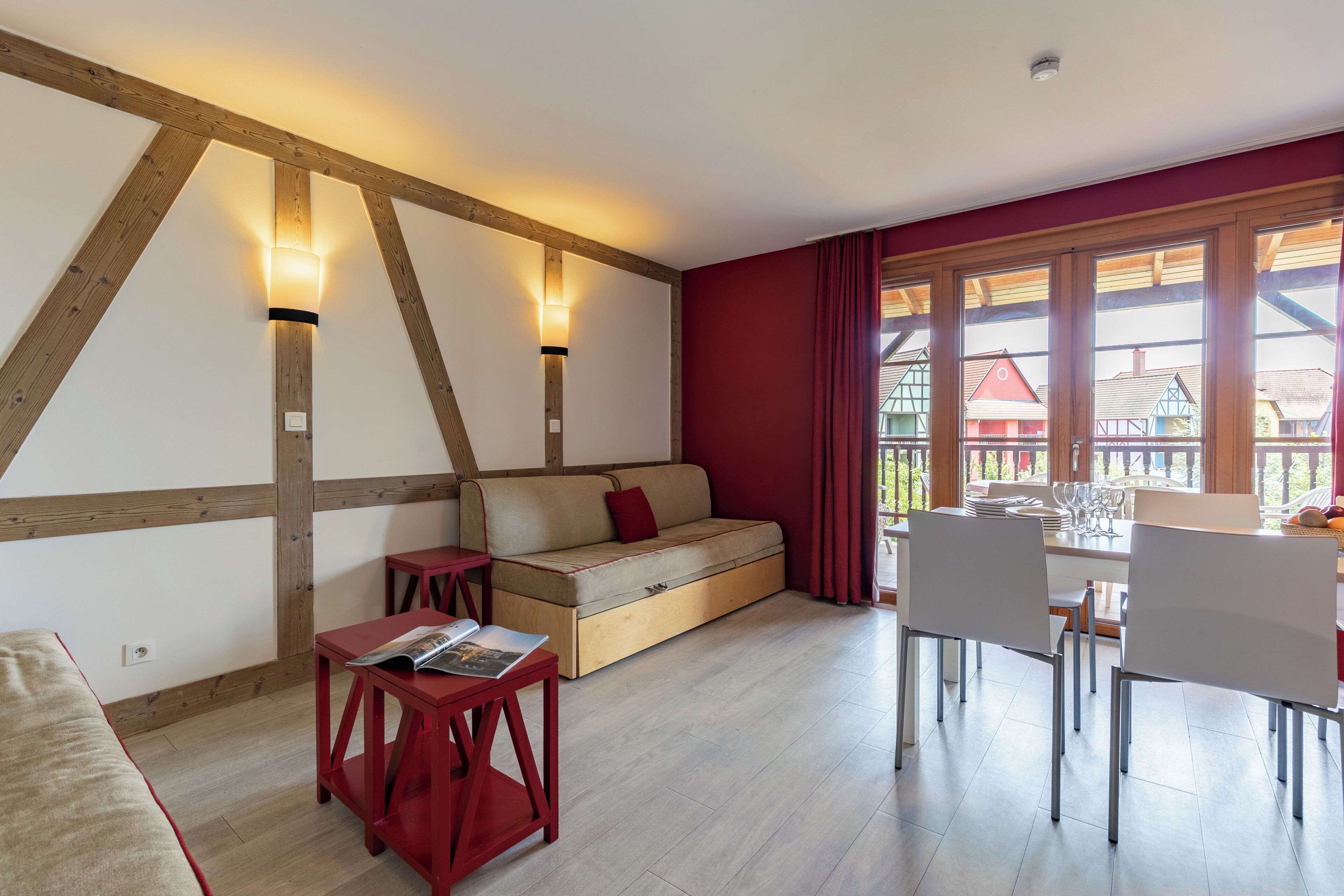 Una habitación acogedora con techo de madera, un sofá, una mesa de comedor con sillas y ventanas amplias con cortinas.