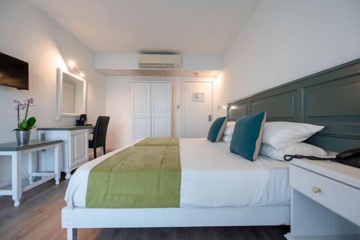 Una habitación de hotel con cama, mesita de noche, silla, escritorio y espejo.