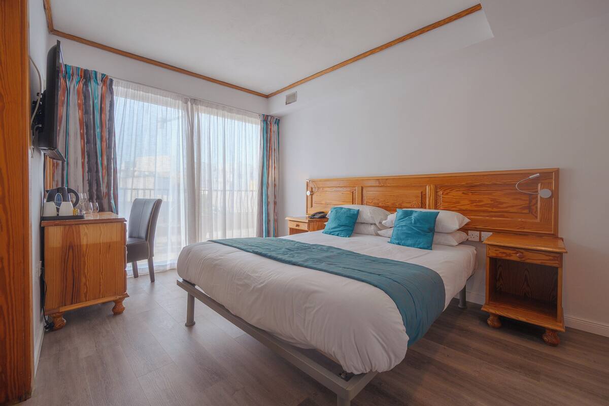Een hotelkamer met een bed, nachtkastjes, een bureau met stoel en een televisie.