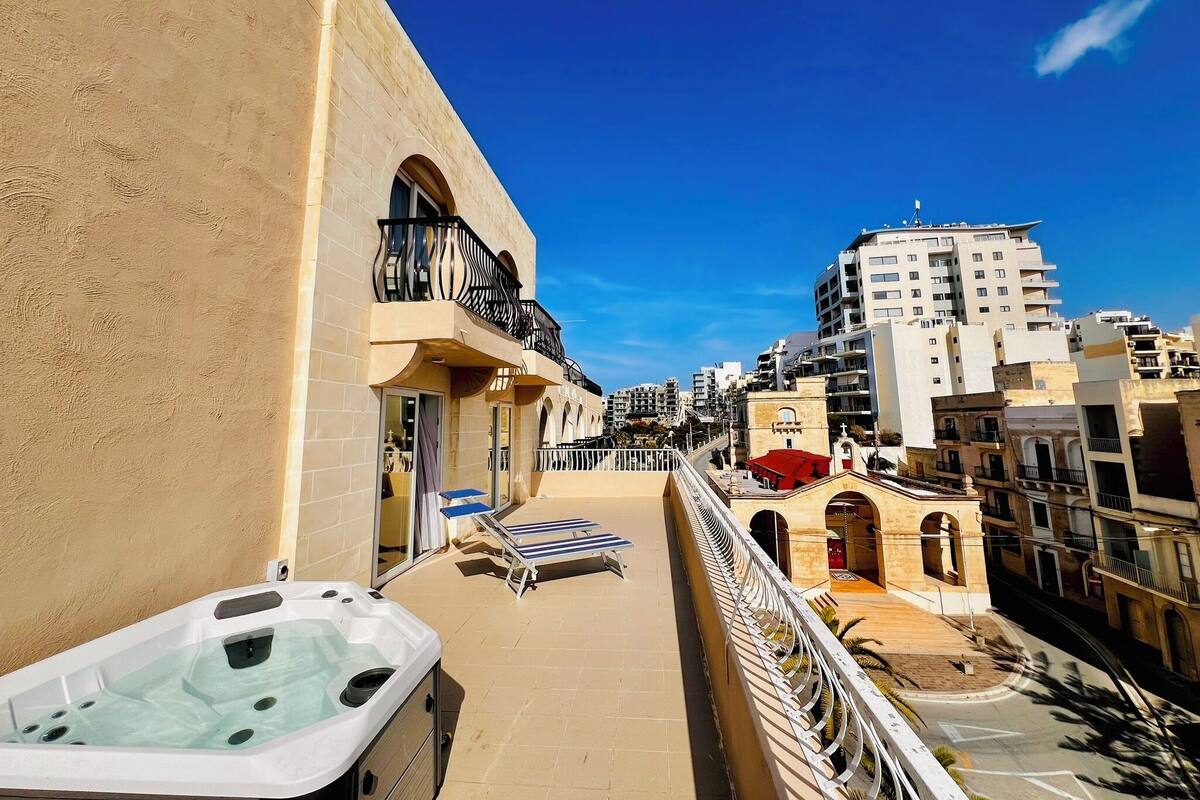 Een balkon met een jacuzzi, lounge stoelen en uitzicht op de stad.