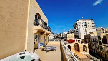 Un balcón con jacuzzi, sillones de descanso y vista a la ciudad.