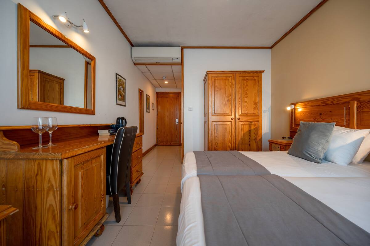 Een hotelkamer met een houten hoofdbord, een groot bed, een bureau met stoel, een kledingkast en een spiegel.