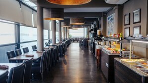 A long dining area with tables and chairs, a buffet on the right, and large windows on the left. - Gillieru Harbour Hotel (St. Paul's Bay)