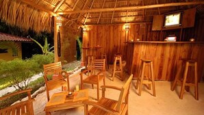 Une cabane en bois avec un toit de chaume, un coin bar avec des tabourets et une table avec des chaises.