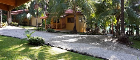 A tropical resort with a gravel pathway, palm trees, and a yellow building with a red roof.