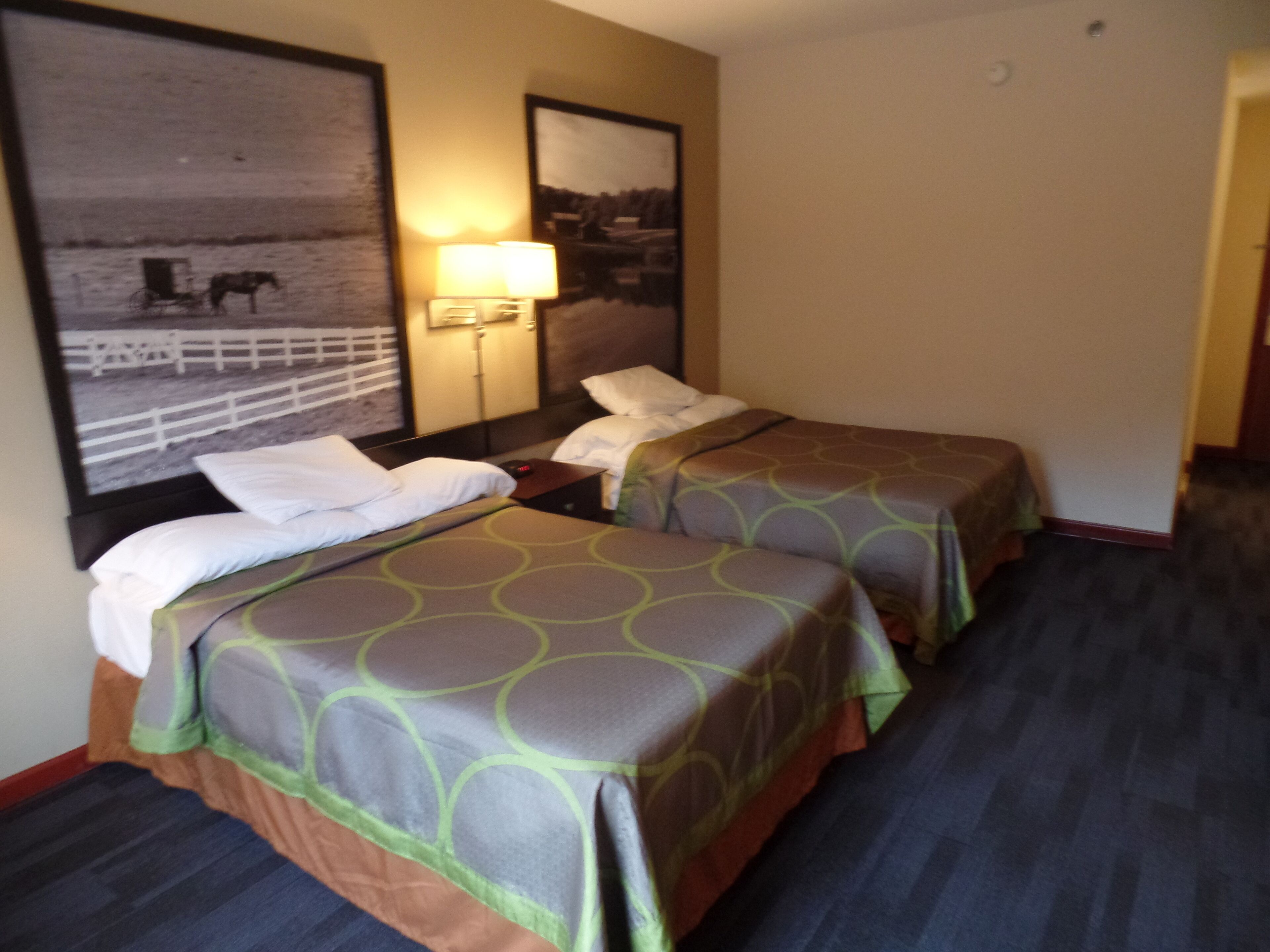 A hotel room with two single beds, a nightstand, a lamp, and a large framed picture on the wall.