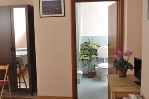 Una habitación con una cama, una silla, una mesa de madera, una planta en maceta y un televisor.