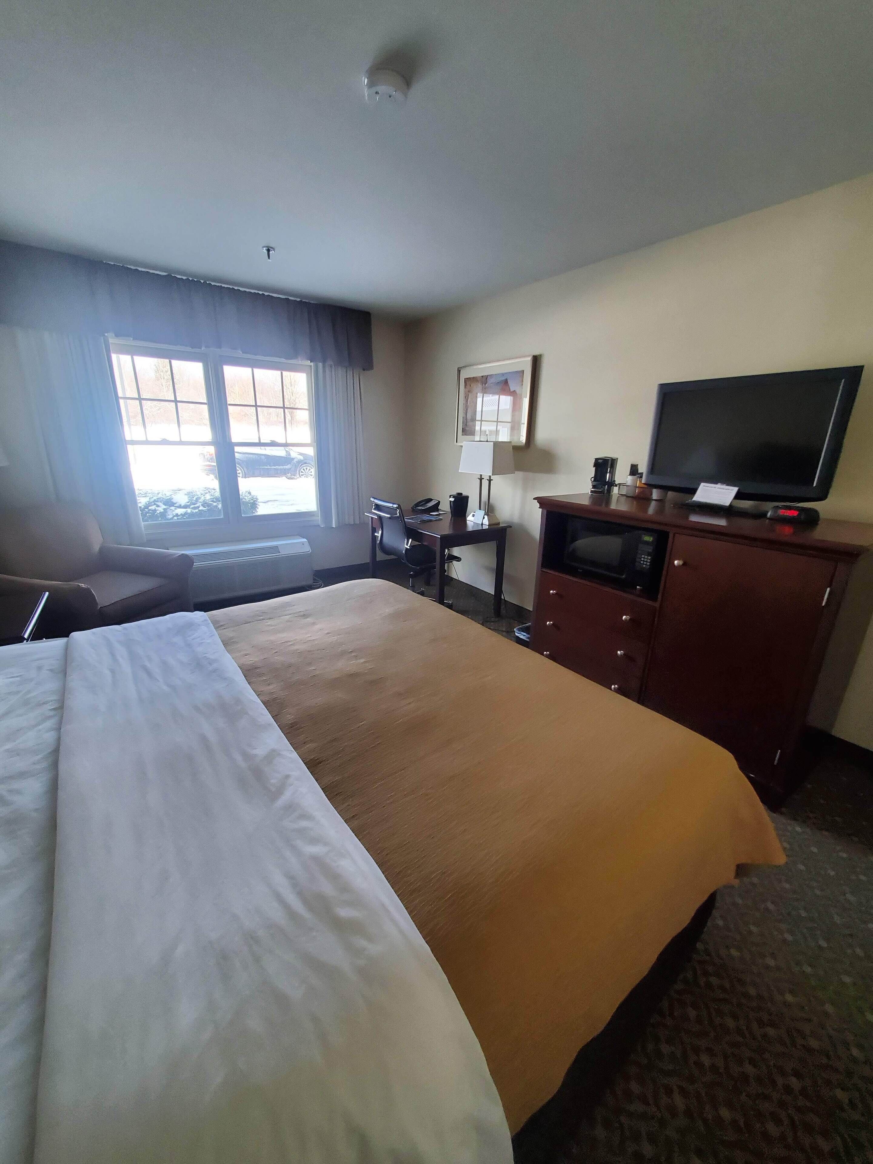 Une chambre d’hôtel avec un grand lit, un bureau avec un ordinateur, une télévision et une fenêtre avec des rideaux.