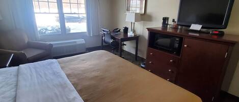 Une chambre d’hôtel avec un grand lit, un bureau avec un ordinateur, une télévision et une fenêtre avec des rideaux.