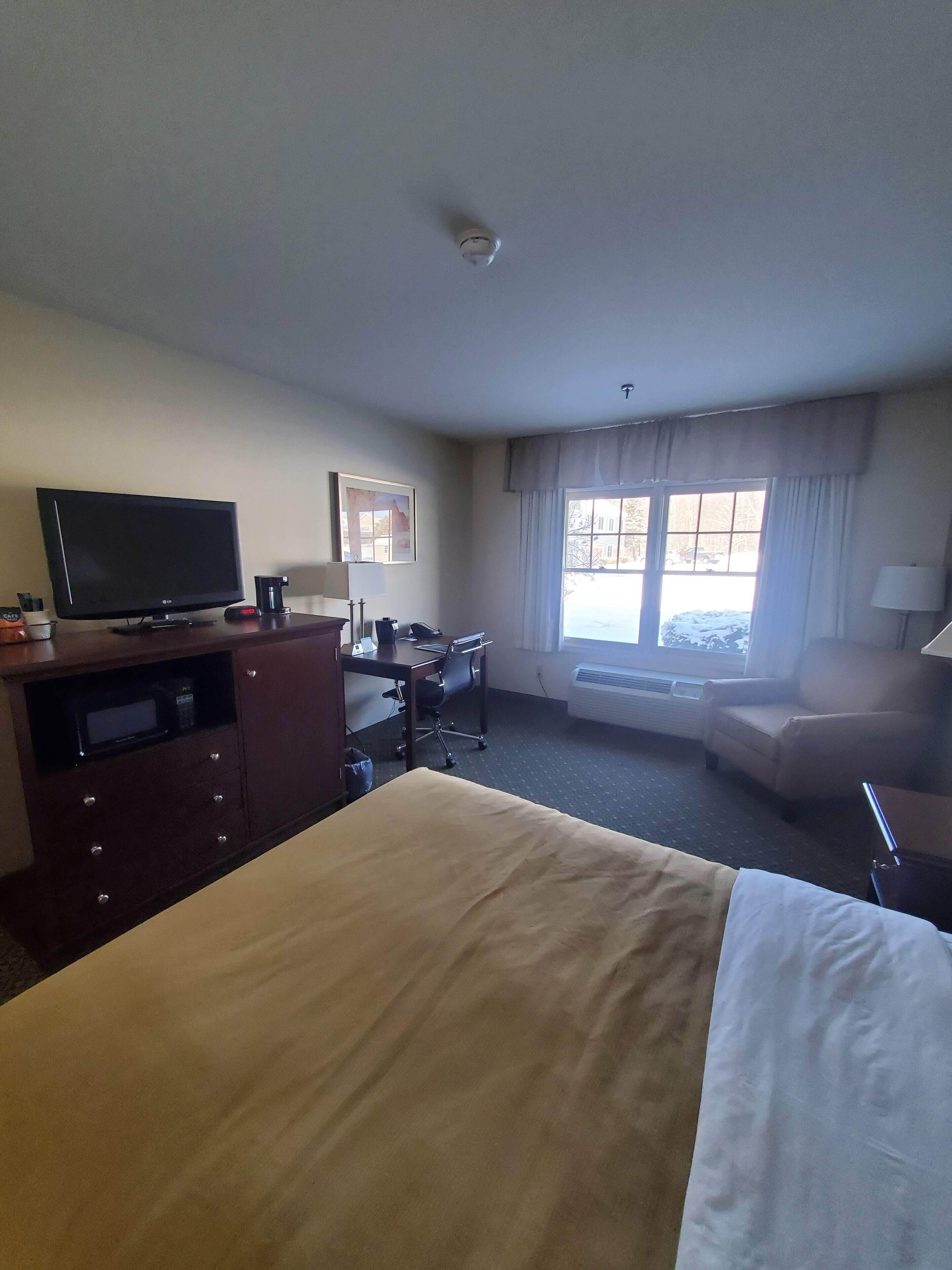 A hotel room with a bed, a desk, a chair, a television, and a window with curtains.
