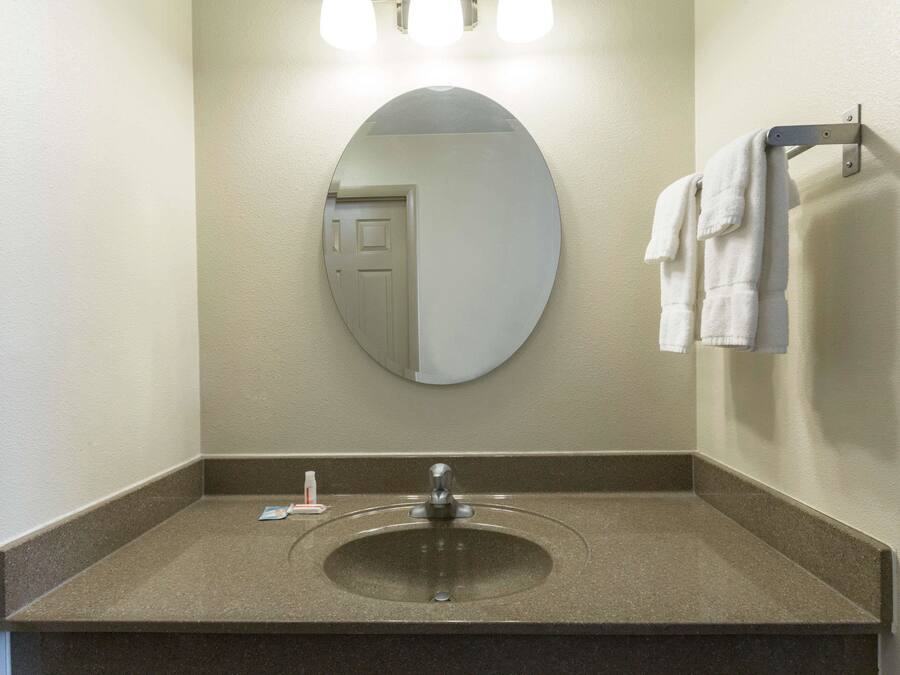Un baño con un espejo redondo, un lavamanos y un perchero para toallas.