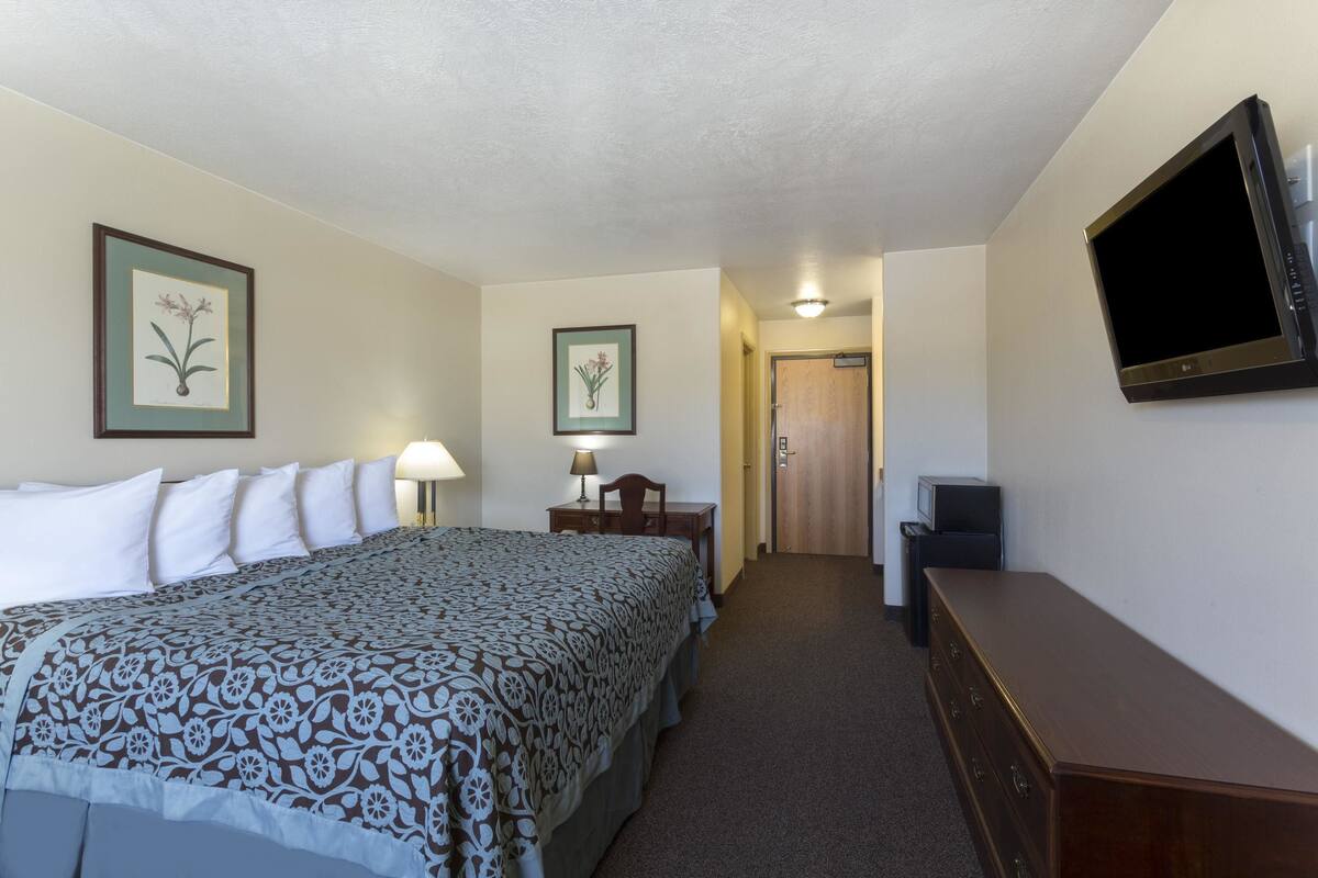 A hotel room with a bed, a desk, a chair, a television, and framed pictures on the wall.