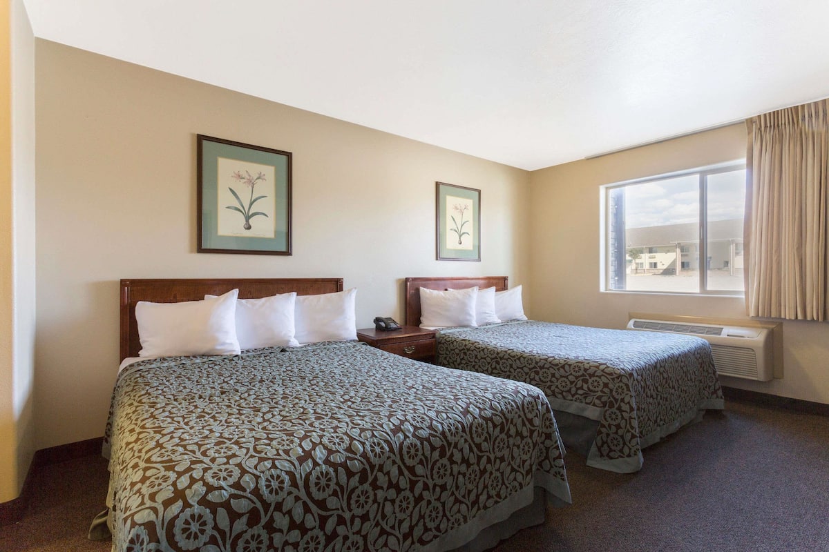 A hotel room with two beds, a large window, and two framed floral pictures on the wall.