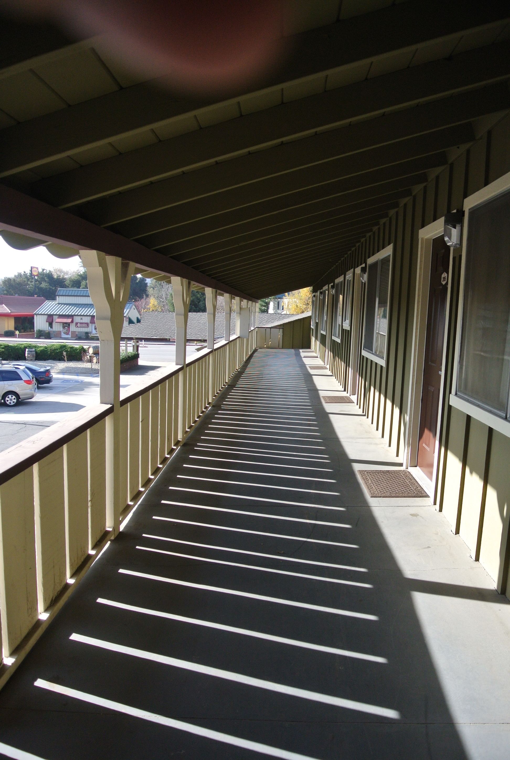 A covered corridor with a row of windows on one side and a parking lot visible outside.