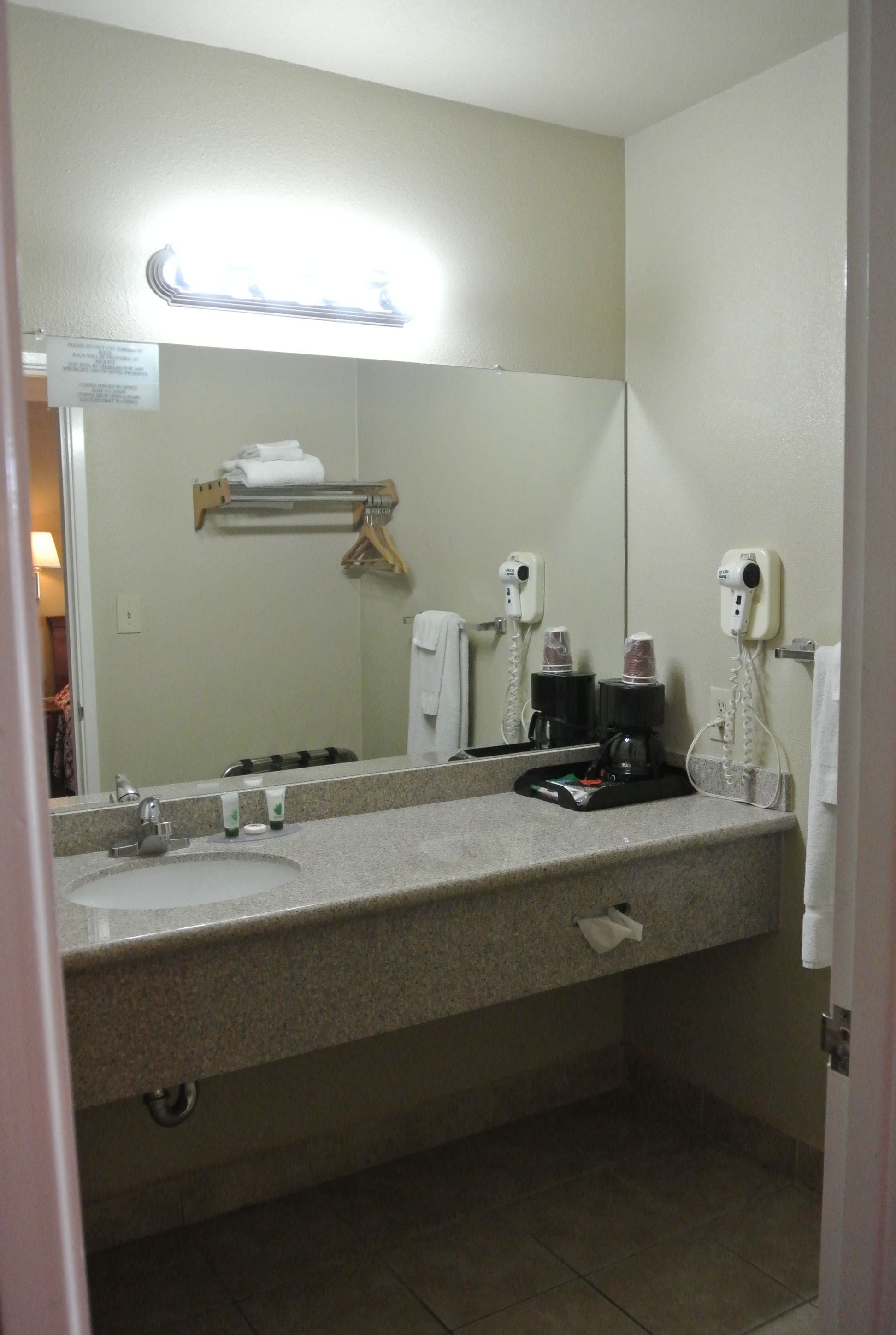A hotel bathroom with a sink, mirror, towel rack, and a coffee machine.