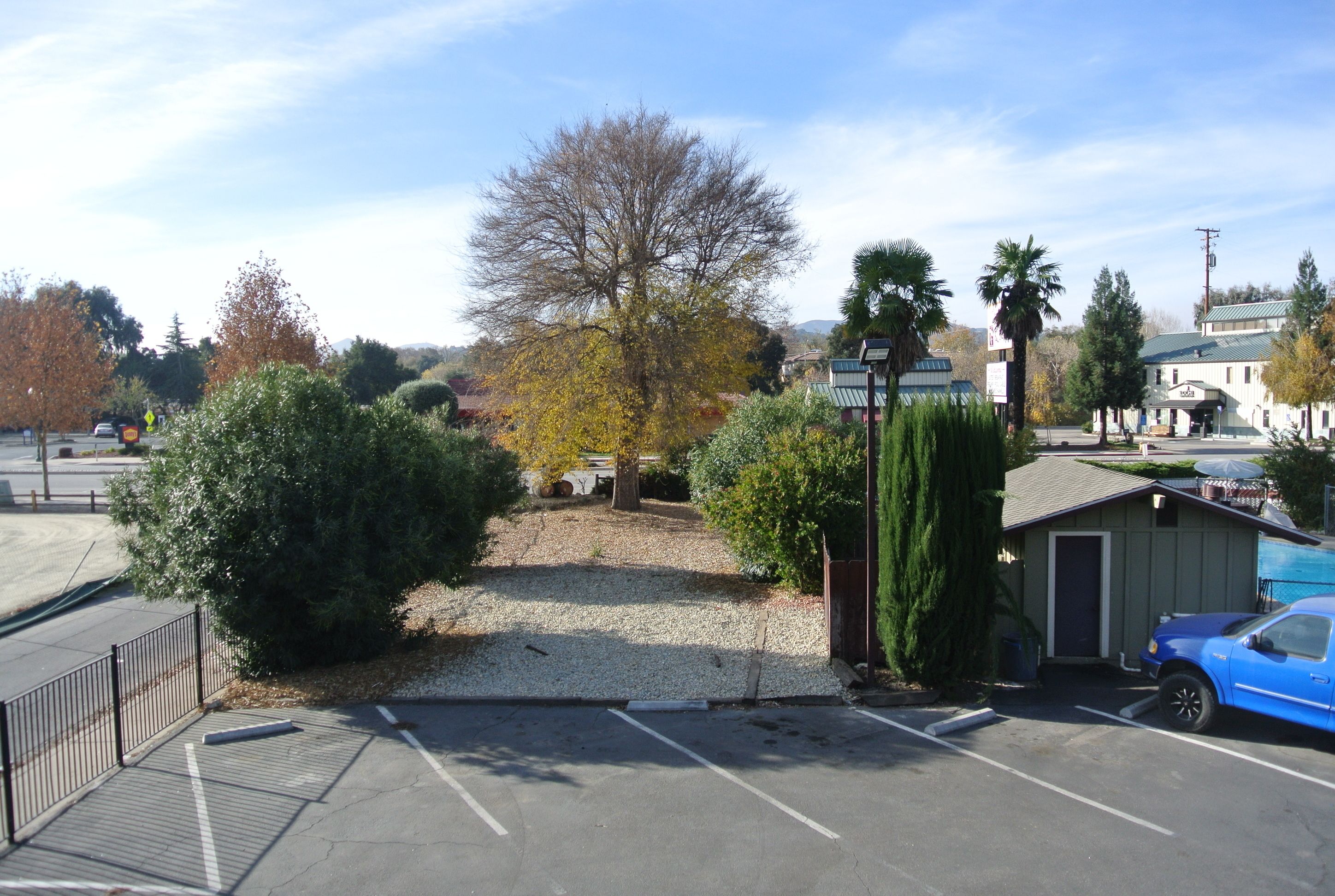 A parking lot with a gravel path leading to a building, surrounded by trees and a clear sky.
