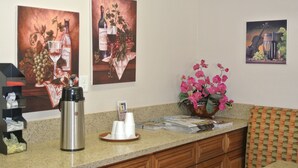 A hotel reception area with a coffee machine, white cups, magazines, and a vase of pink flowers.