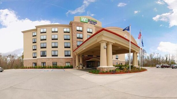 A hotel with a large entrance, multiple floors, and a flag in front. - Holiday Inn Express & Suites Laplace by IHG (LaPlace)