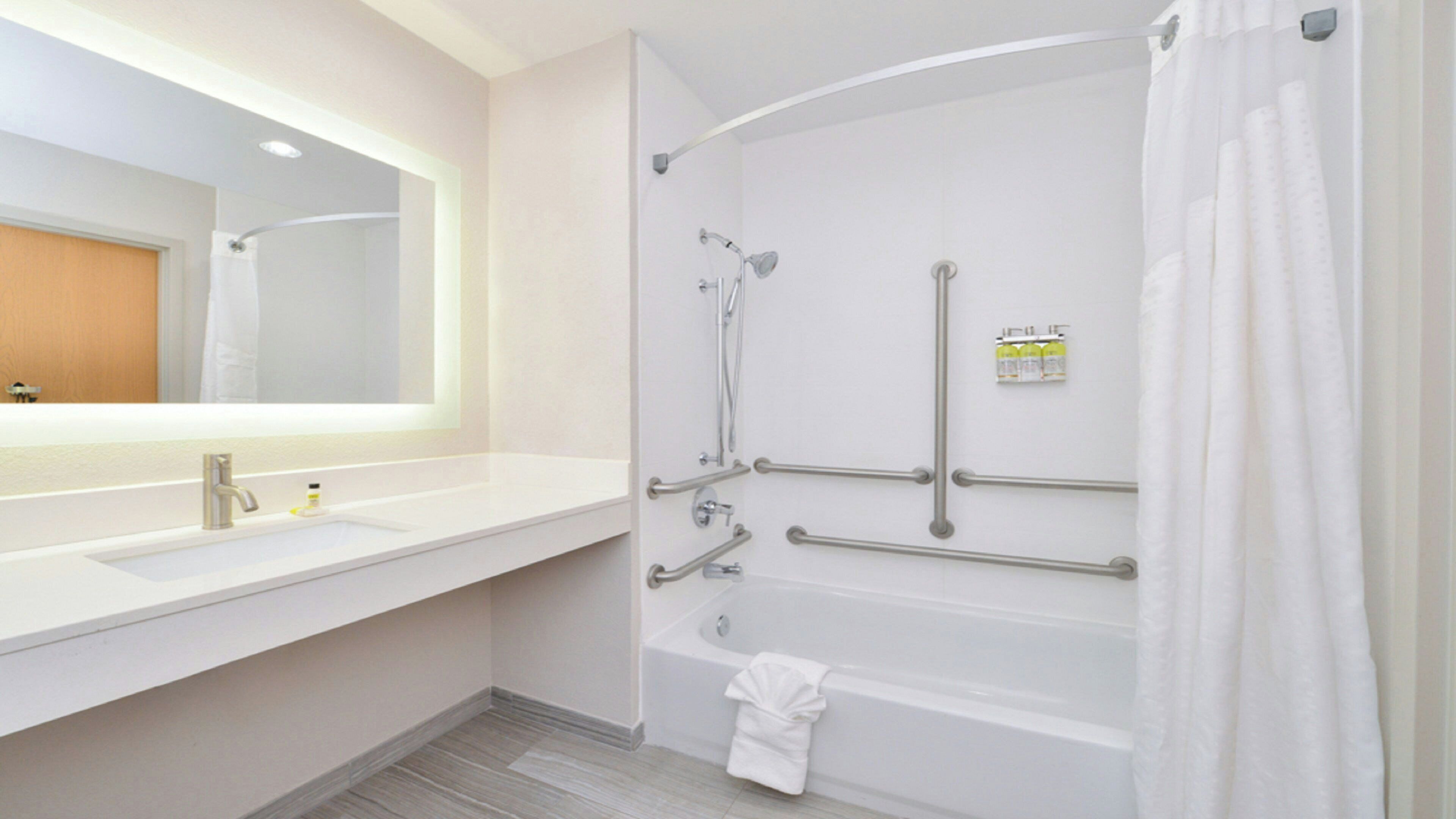 Un baño moderno con lavamanos, espejo y bañera blancos.