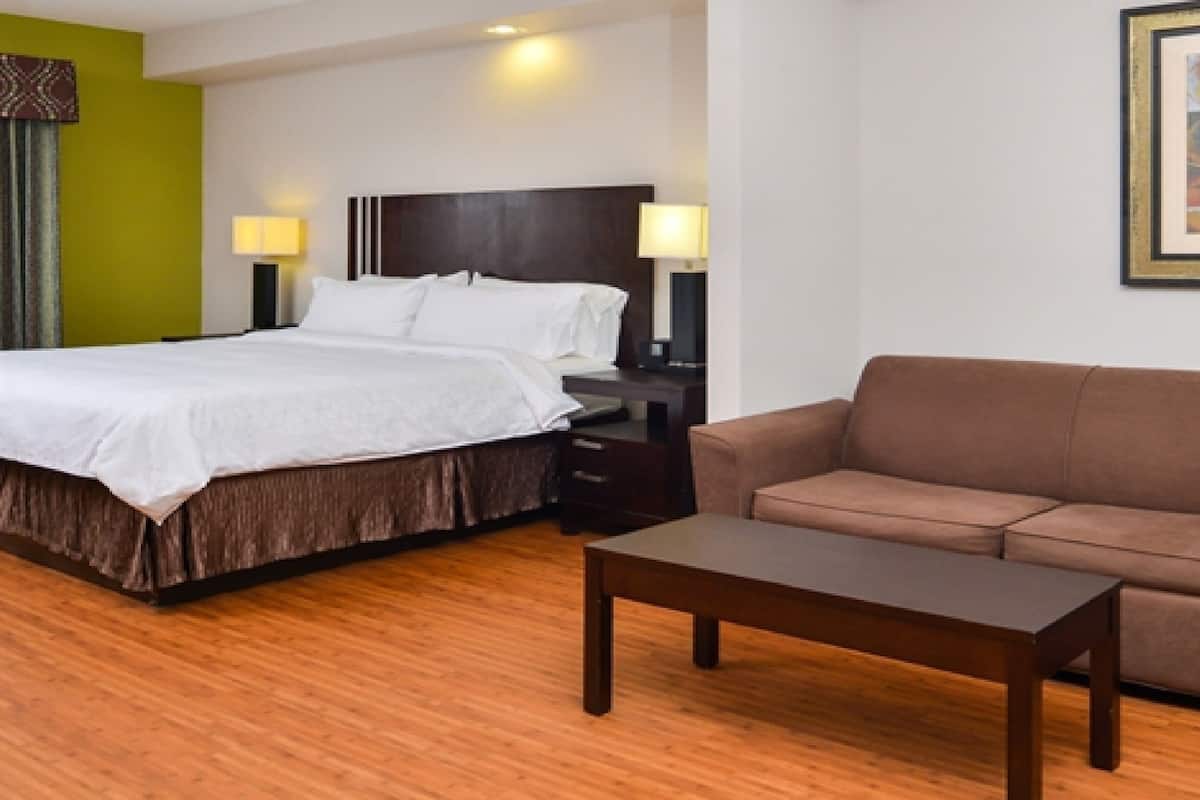 Una habitación de hotel con una cama, un sofá marrón, una mesita de madera y dos lámparas de noche.