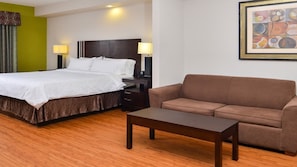 Una habitación de hotel con una cama, un sofá marrón, una mesita de madera y dos lámparas de noche.