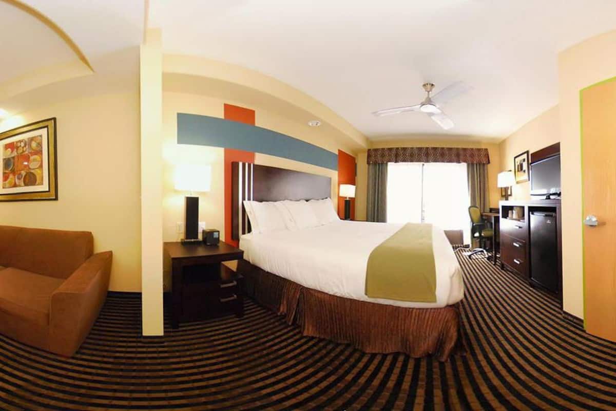 Una habitación de hotel con cama, escritorio, silla, televisor y armario.