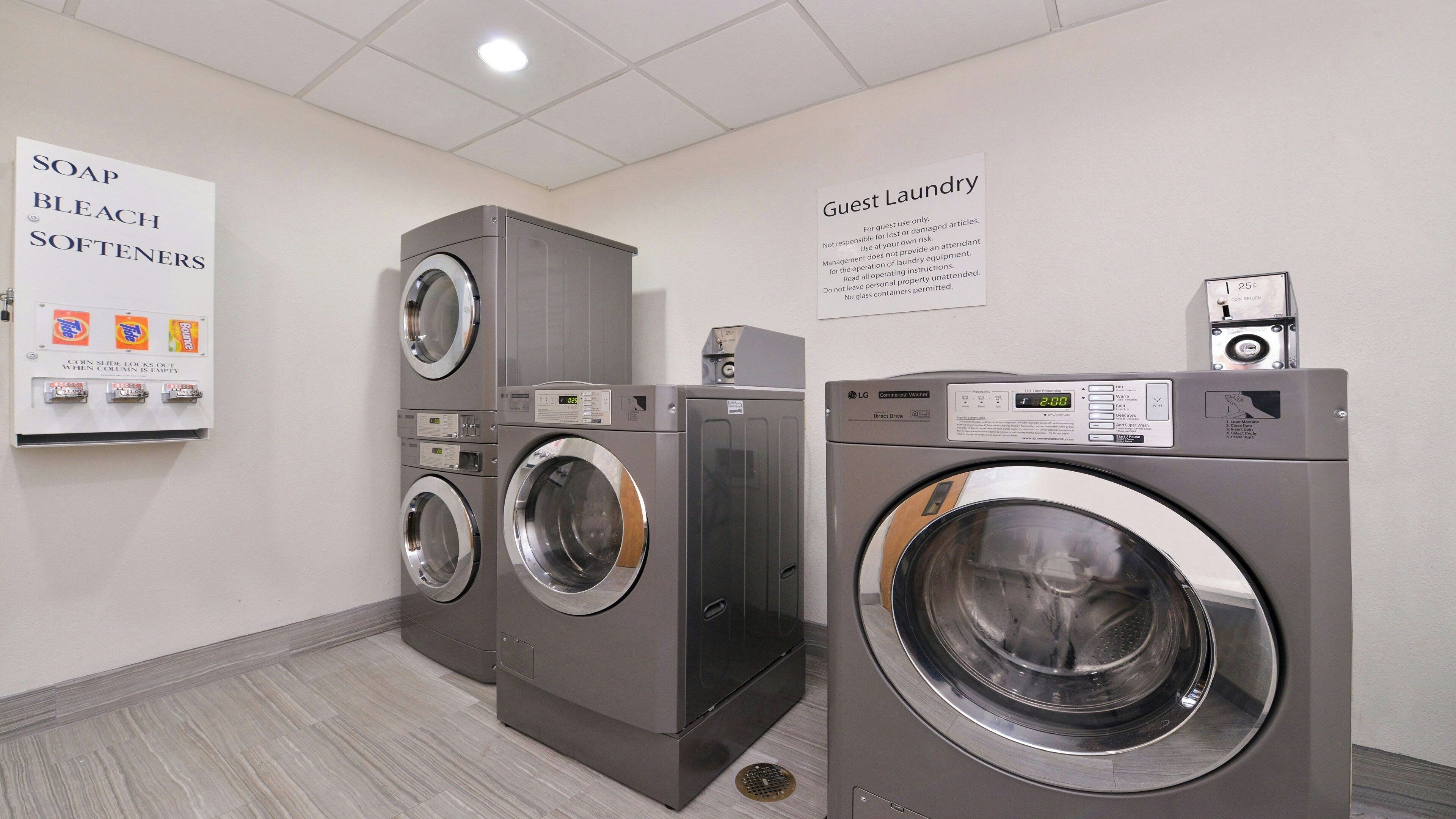 A laundry facility with multiple washers and dryers, a coin-operated soap and bleach dispenser, and a guest laundry sign.