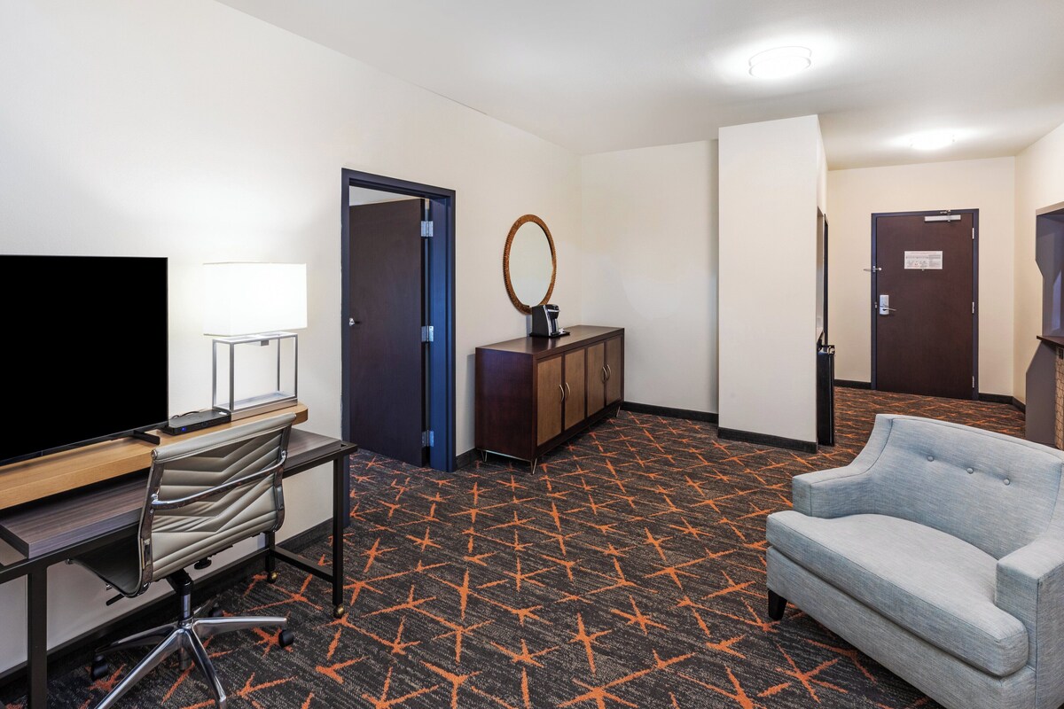 A hotel room with a desk, chair, TV, wardrobe, and a sofa.