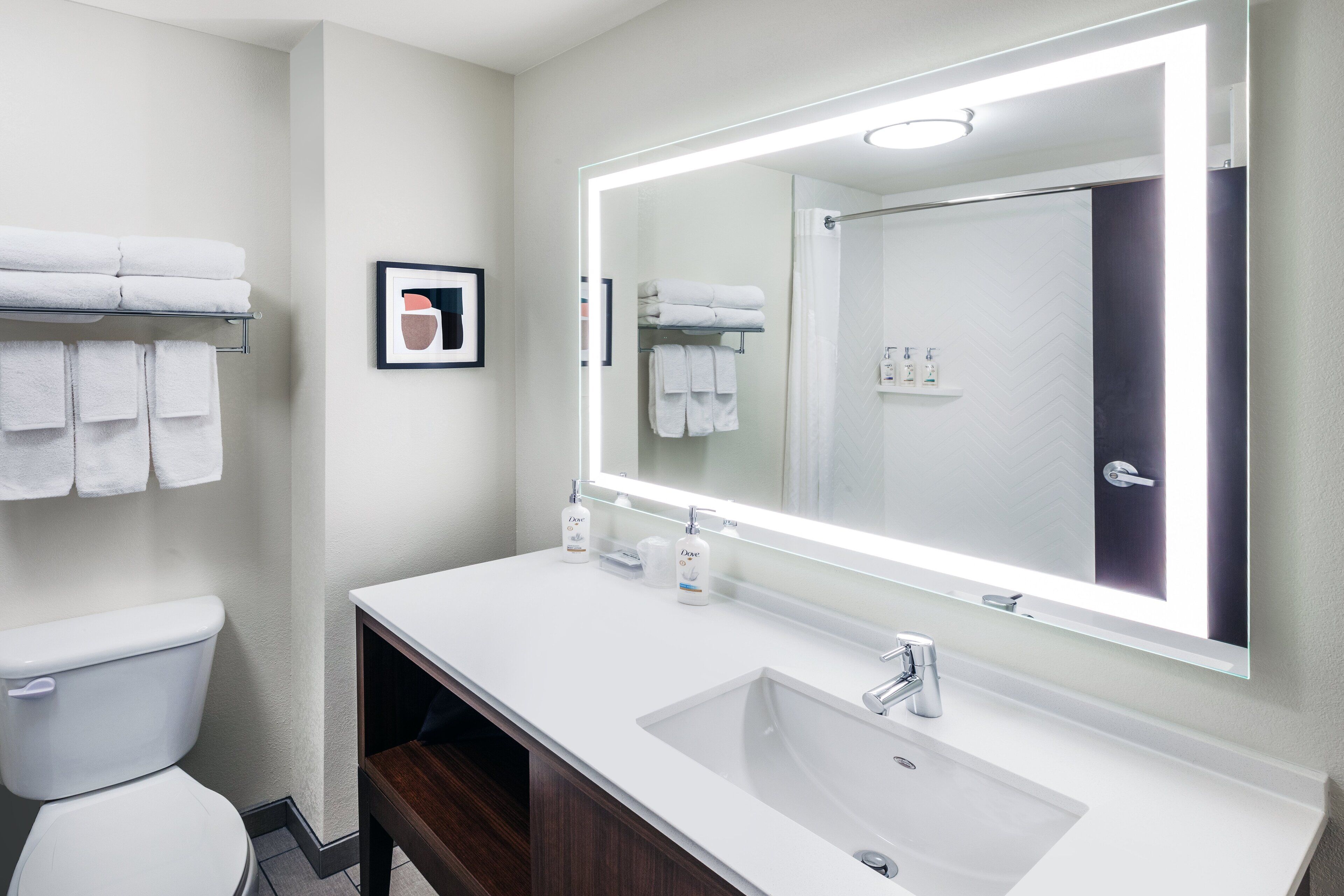 A modern bathroom with a white sink, a large mirror, and neatly arranged towels.