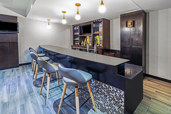 A modern bar area with a long counter, bar stools, and a television screen. - Holiday Inn Stillwater - University West by IHG (Stillwater)