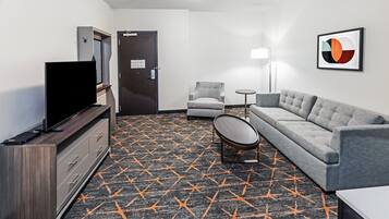 A hotel room with a flat-screen TV, a sofa, a chair, a small table, and a patterned carpet.