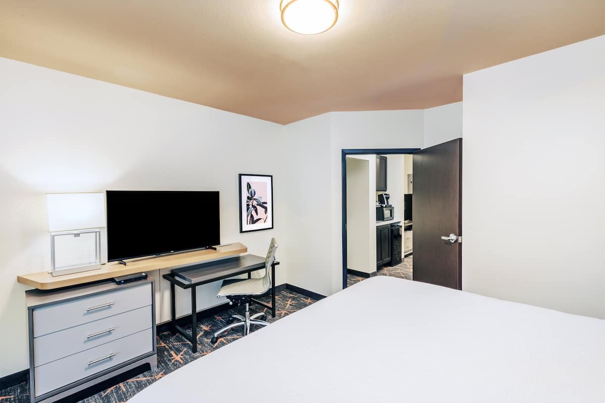 A hotel room with a bed, desk, chair, TV, and a framed picture on the wall.