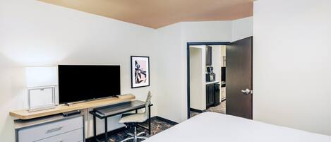 A hotel room with a bed, desk, chair, TV, and a framed picture on the wall.