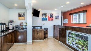 A modern kitchen with dark wooden cabinets, a coffee machine, and a large screen displaying a forest scene. - Motel 6 Astoria, OR (Astoria)