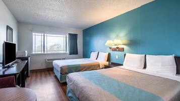 A hotel room with two beds, a desk with a TV, and a window with curtains.