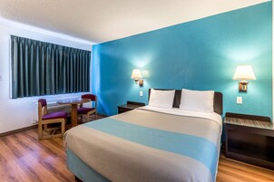 Habitación de hotel con una cama grande, dos mesitas de noche con lámparas, una pequeña mesa con sillas y una ventana con cortinas.