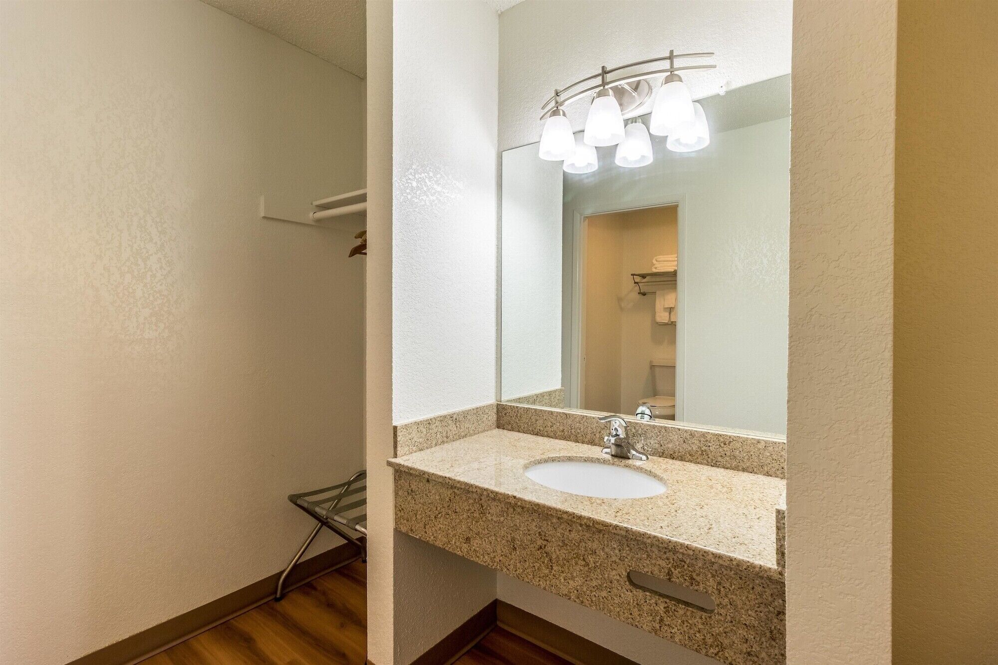 A bathroom with a granite countertop, a white sink, and a mirror with lights.