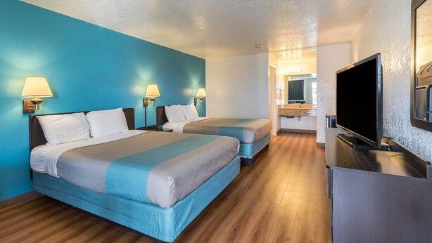 A hotel room with two beds, a television, a desk, and a bathroom visible in the background. - Motel 6 Astoria, OR (Astoria)