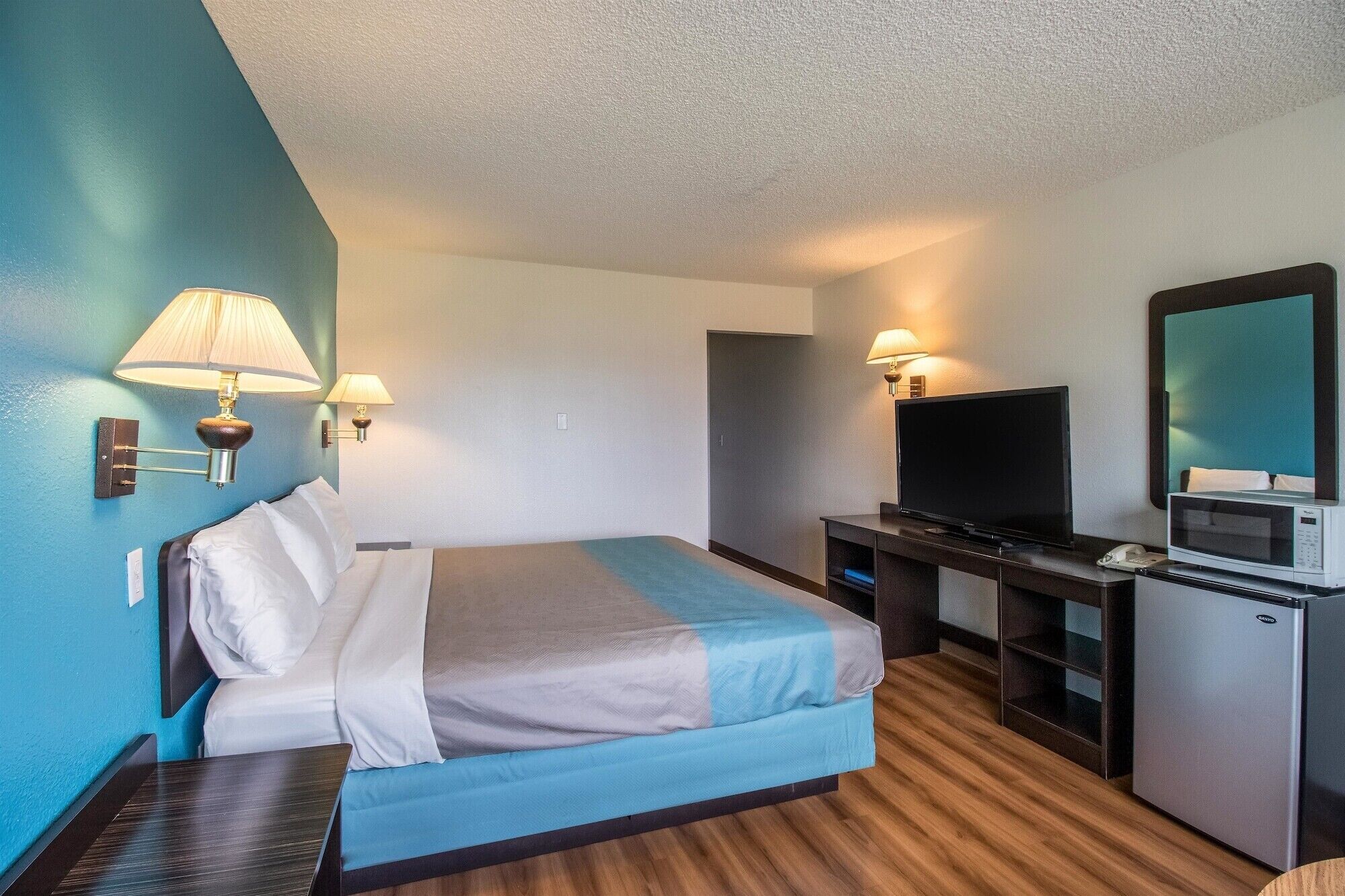 A hotel room with a bed, a desk with a television, a microwave, and a minibar.
