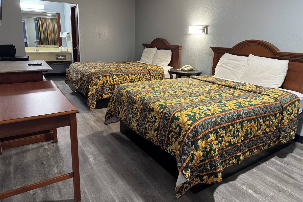 A hotel room with two beds, a desk, and a mirror.