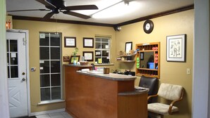 A reception area with a wooden counter, a black office chair, a ceiling fan, and a clock on the wall. - Claremore Motor Inn (Claremore)